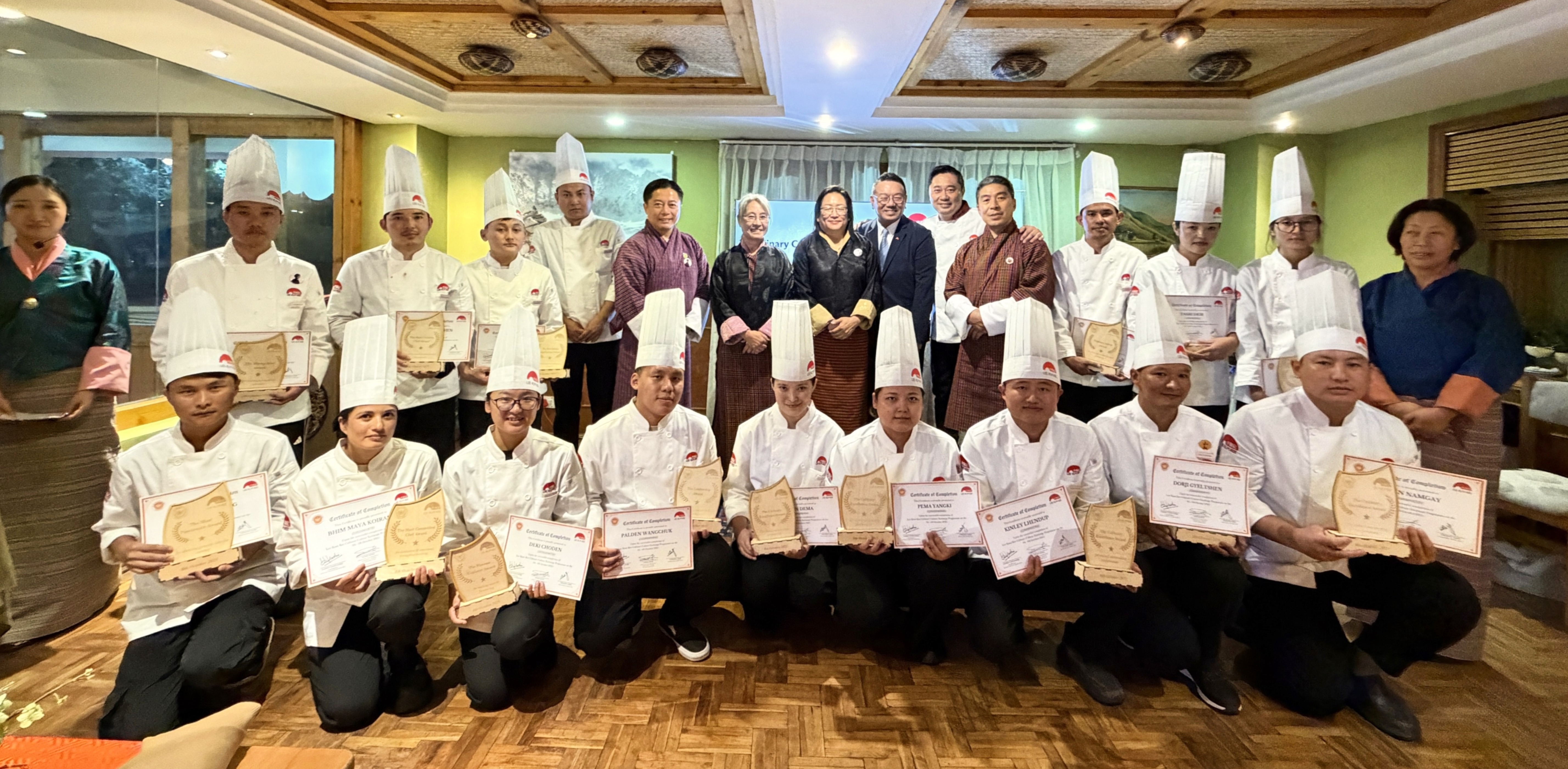 Zimpon Wom Sonam Thinley, Steering Committee Member, Desuung Skilling Programme (back row, sixth from left), Dasho Tashi Wangmo, Secretary of the Ministry of Industry, Commerce and Employment, Royal Government of Bhutan (back row, seventh from left), Dasho Kesang Chuki Dorjee, Eminent Member, National Council of Bhutan, Steering Committee Member, Desuung Skilling Programme (back row, eighth from right), Karma Tshering, Executive Director, Post Skilling, Steering Committee Member, Desuung Skilling Programme (back row, fifth from right), Dodie Hung, Executive Vice President – Corporate Affairs of Lee Kum Kee Sauce (back row, seventh from right), and Chef Vincent Liew, Executive Chef at The Star Sydney (back row, sixth from right), present certificates to young chefs of the culinary culture exchange programme.